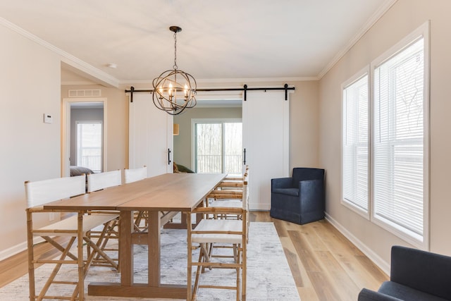 dining space with ornamental molding, a barn door, a wealth of natural light, and light hardwood / wood-style floors