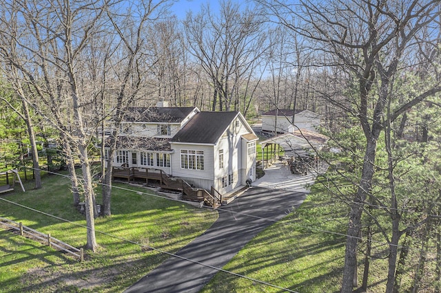 view of front facade featuring aphalt driveway, a chimney, a shingled roof, a deck, and a front lawn