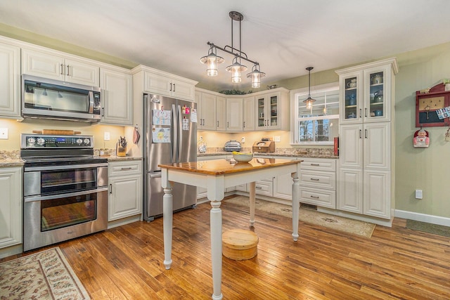 kitchen featuring stainless steel appliances, light wood finished floors, glass insert cabinets, and decorative light fixtures