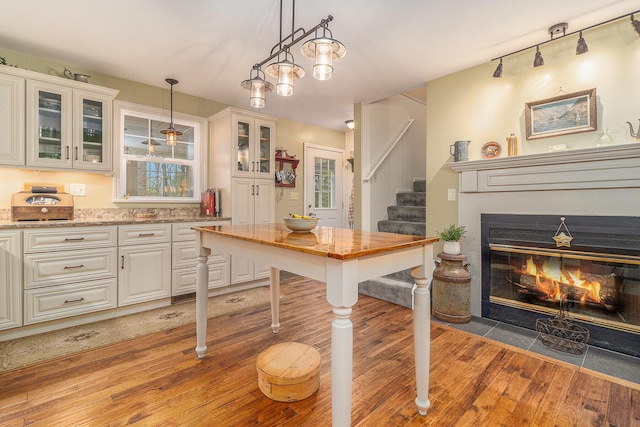 kitchen with hanging light fixtures, light stone counters, glass insert cabinets, and white cabinetry