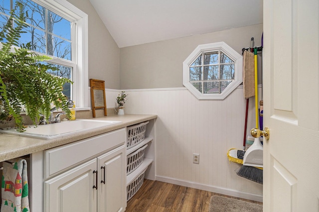 bathroom with lofted ceiling, wainscoting, a sink, and wood finished floors