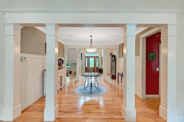 foyer entrance featuring light wood finished floors, a wainscoted wall, ornamental molding, a decorative wall, and ornate columns