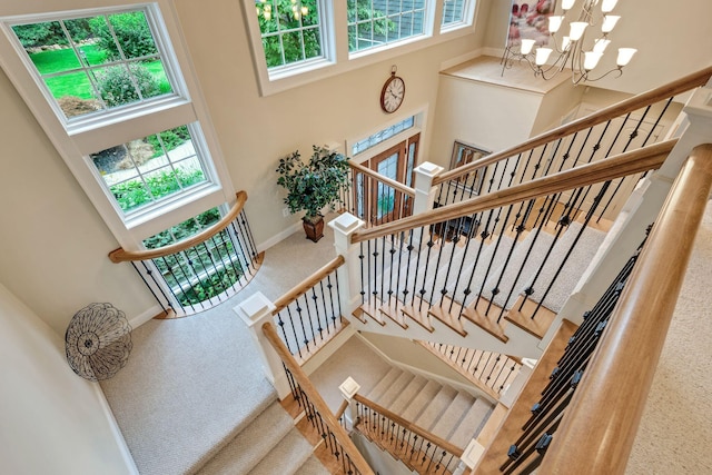 stairs featuring a chandelier, carpet flooring, baseboards, and a towering ceiling