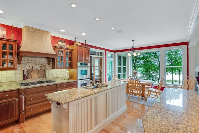 kitchen featuring glass insert cabinets, custom range hood, ornamental molding, appliances with stainless steel finishes, and light wood-style floors