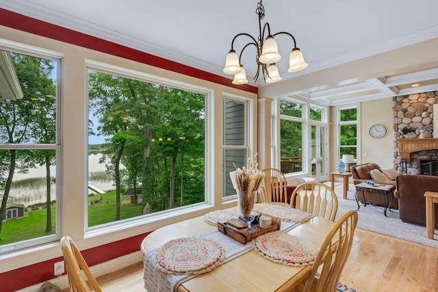 dining area featuring a stone fireplace, an inviting chandelier, light wood-style floors, and coffered ceiling