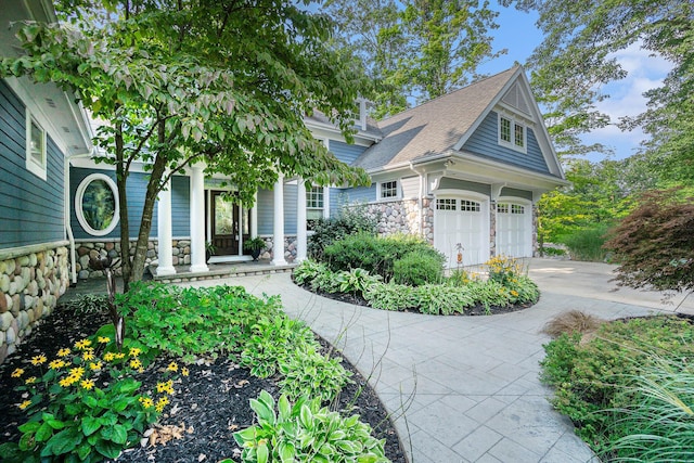 view of front facade featuring stone siding, a porch, roof with shingles, concrete driveway, and a garage