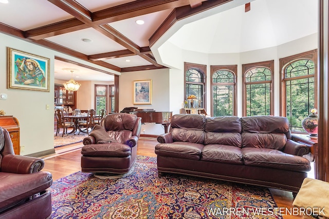 living room with beam ceiling, coffered ceiling, an inviting chandelier, and light wood-type flooring