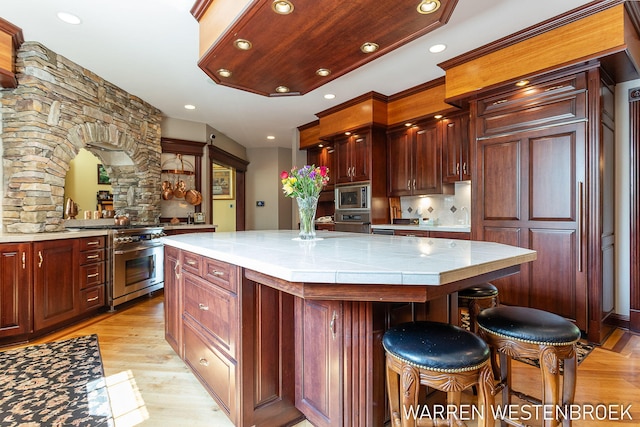 kitchen featuring a breakfast bar, appliances with stainless steel finishes, tile counters, a kitchen island, and light wood-type flooring