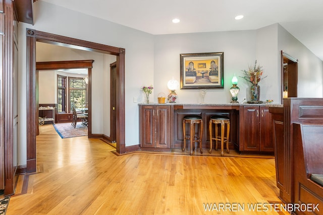 bar with light stone counters and light hardwood / wood-style floors