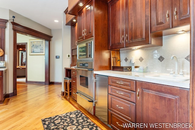 kitchen featuring tasteful backsplash, appliances with stainless steel finishes, sink, and light hardwood / wood-style flooring