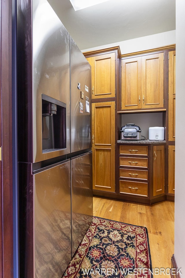 kitchen with stainless steel refrigerator with ice dispenser, light hardwood / wood-style flooring, and dark stone countertops