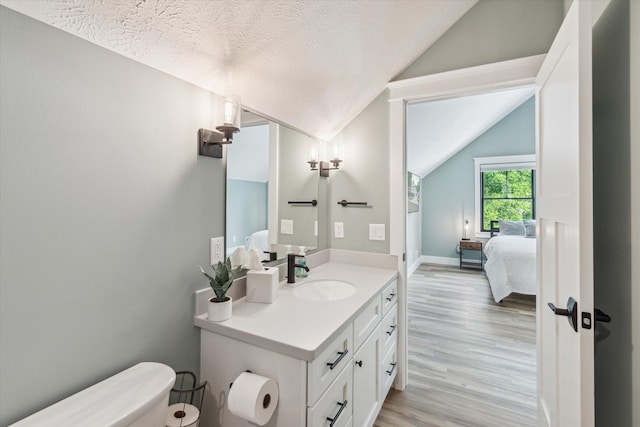 bathroom featuring lofted ceiling, hardwood / wood-style floors, vanity, a textured ceiling, and toilet