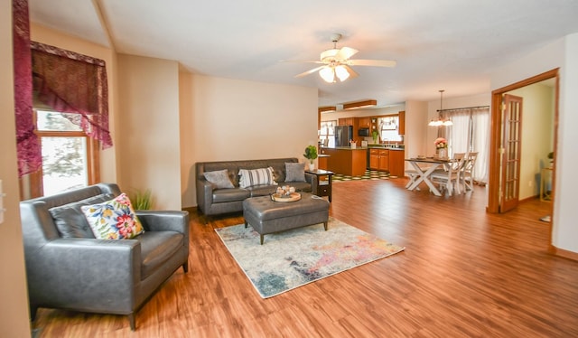 living room with a wealth of natural light, sink, wood-type flooring, and ceiling fan with notable chandelier