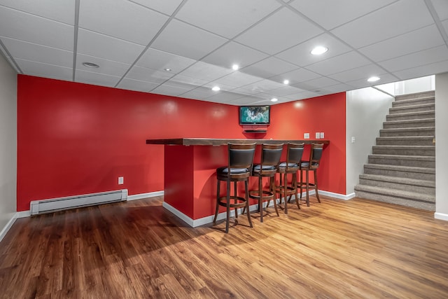 bar featuring a baseboard radiator, hardwood / wood-style flooring, and a paneled ceiling