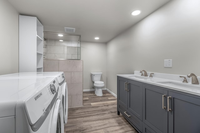 bathroom featuring tile walls, washer and clothes dryer, hardwood / wood-style floors, dual bowl vanity, and toilet