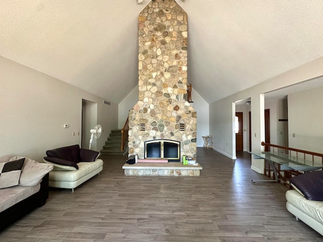 living room with lofted ceiling, hardwood / wood-style floors, a stone fireplace, and a textured ceiling