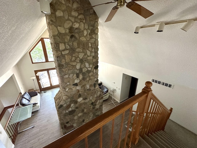 stairway featuring lofted ceiling, wood finished floors, visible vents, and a textured ceiling