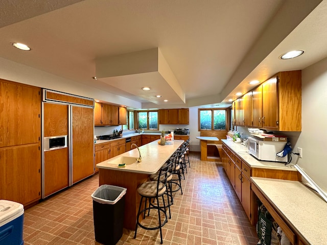 kitchen featuring a breakfast bar area, a center island with sink, and paneled built in fridge