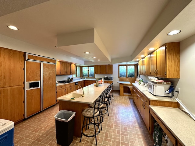 kitchen featuring brown cabinetry, recessed lighting, a breakfast bar area, and paneled built in fridge