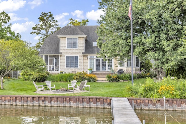 back of house featuring a yard, a water view, a fire pit, and roof with shingles