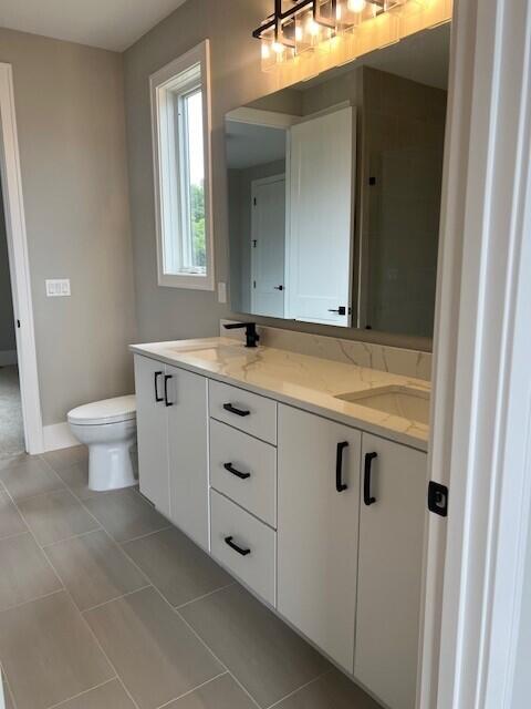 full bath with a sink, toilet, double vanity, and tile patterned flooring