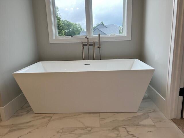 bathroom featuring a freestanding tub, baseboards, and marble finish floor