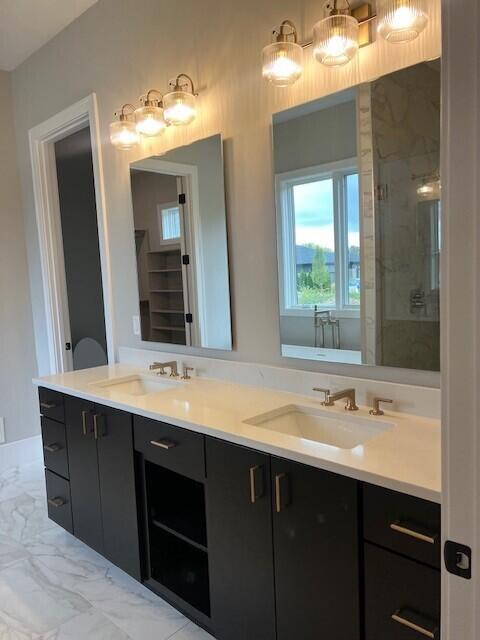 full bath featuring double vanity, marble finish floor, a stall shower, and a sink