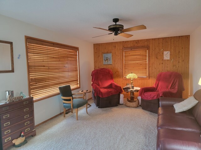 carpeted living room featuring wooden walls and ceiling fan