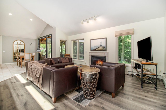 living room with a tile fireplace, rail lighting, light wood-type flooring, and high vaulted ceiling