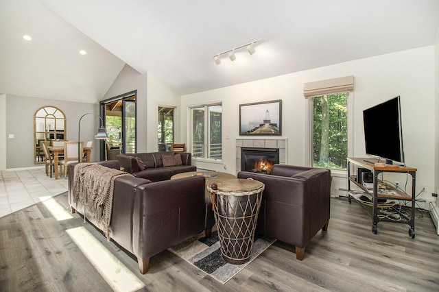 living area with light wood finished floors, track lighting, lofted ceiling, recessed lighting, and a tile fireplace