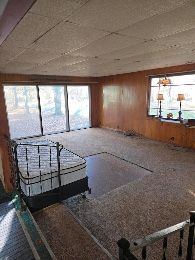 carpeted bedroom with wood walls and a paneled ceiling