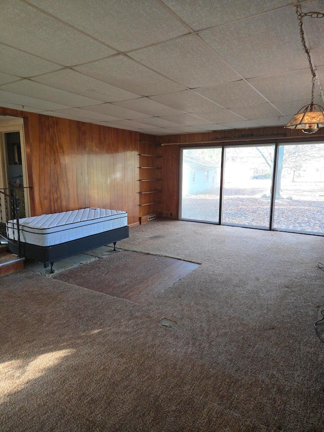 unfurnished bedroom featuring wood walls, a paneled ceiling, and carpet floors