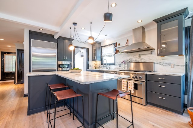 kitchen featuring plenty of natural light, built in appliances, wall chimney exhaust hood, and a kitchen bar