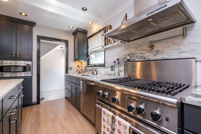 kitchen with wall chimney range hood, backsplash, stainless steel appliances, light hardwood / wood-style floors, and sink