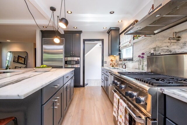 kitchen with tasteful backsplash, light wood-type flooring, light stone countertops, hanging light fixtures, and built in appliances