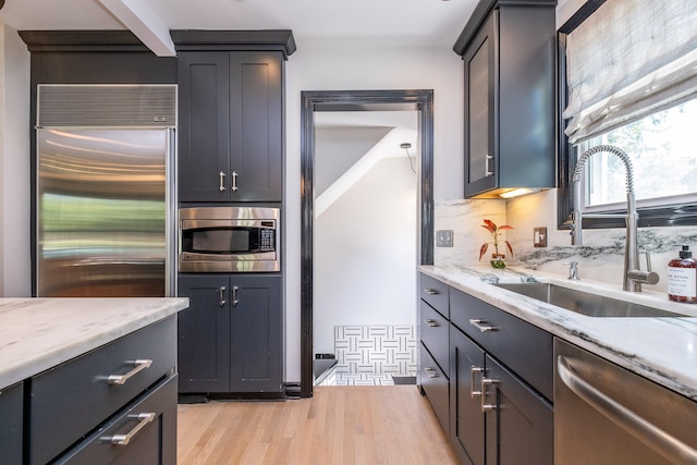 kitchen with built in appliances, sink, light stone countertops, and light hardwood / wood-style flooring