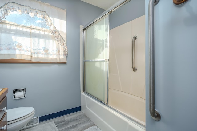 full bathroom with combined bath / shower with glass door, vanity, hardwood / wood-style flooring, and toilet