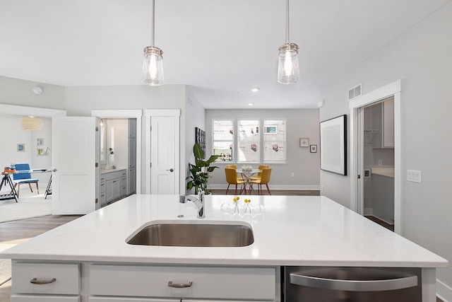 kitchen with light stone counters, pendant lighting, and an island with sink