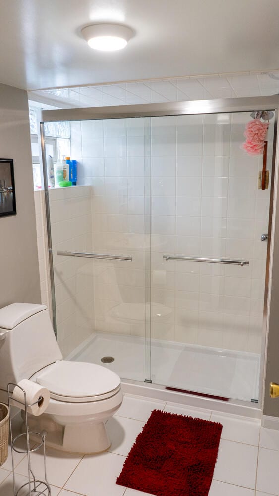 bathroom with a shower with door, tile patterned flooring, and toilet