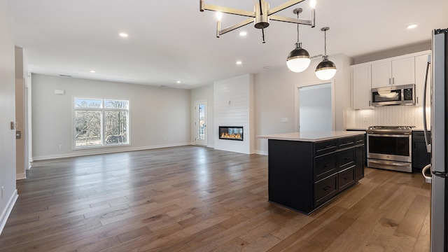 kitchen with a large fireplace, white cabinetry, hardwood / wood-style floors, a kitchen island, and appliances with stainless steel finishes