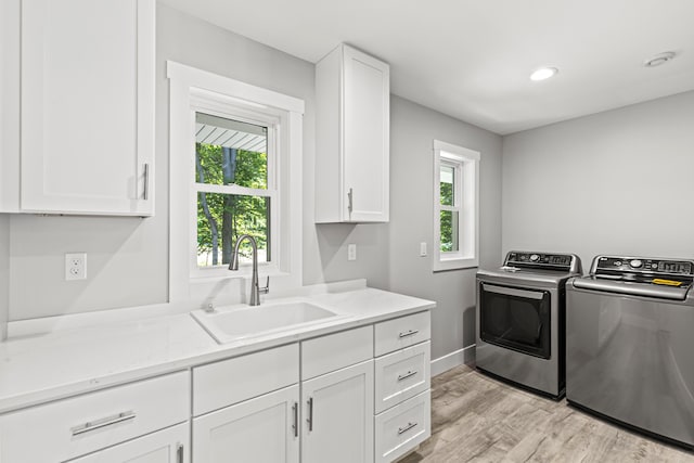 washroom with washer and dryer, sink, cabinets, and light hardwood / wood-style floors