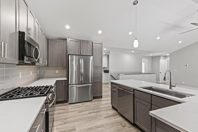 kitchen with appliances with stainless steel finishes, tasteful backsplash, sink, hanging light fixtures, and light hardwood / wood-style flooring