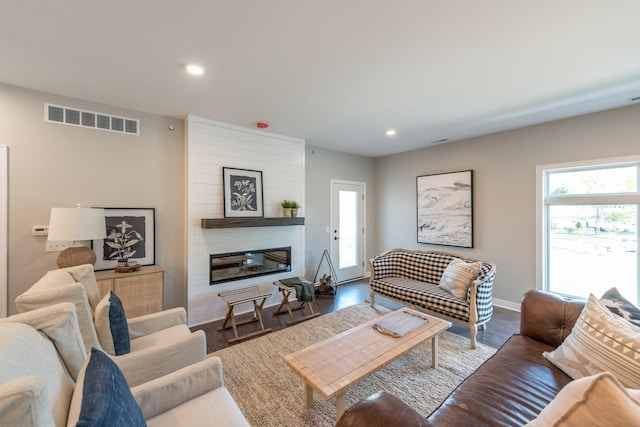 living room with a large fireplace, dark hardwood / wood-style flooring, and plenty of natural light