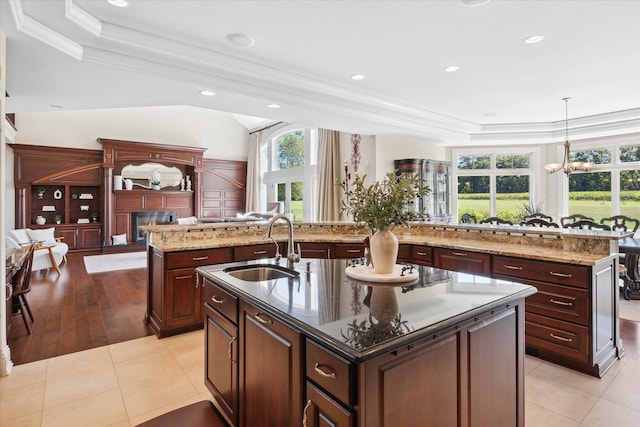 kitchen with pendant lighting, an inviting chandelier, sink, light tile patterned floors, and a center island with sink