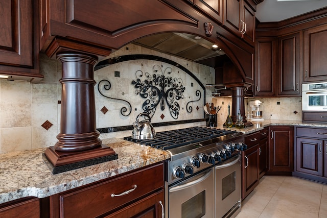 kitchen with stainless steel appliances, ornate columns, tasteful backsplash, light tile patterned flooring, and light stone counters