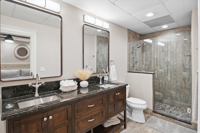 bathroom featuring toilet, vanity, a drop ceiling, and a shower with shower door