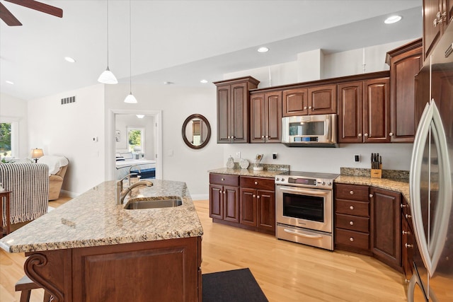 kitchen with decorative light fixtures, sink, stainless steel appliances, and an island with sink