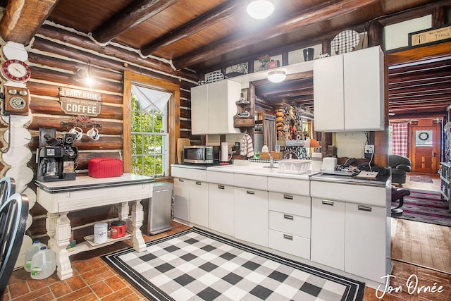 kitchen with rustic walls, sink, wood ceiling, beamed ceiling, and white cabinets