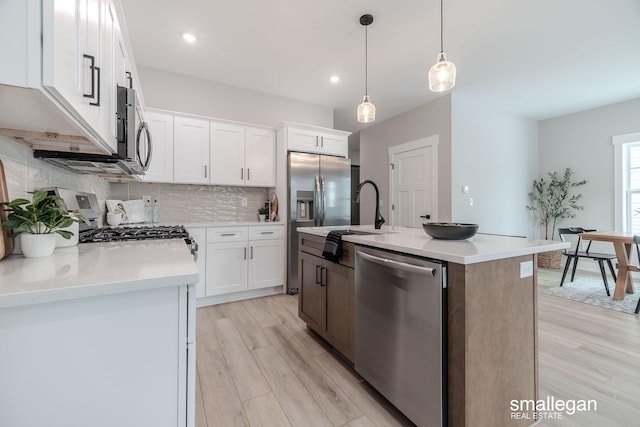 kitchen featuring decorative light fixtures, a center island with sink, white cabinets, stainless steel appliances, and backsplash