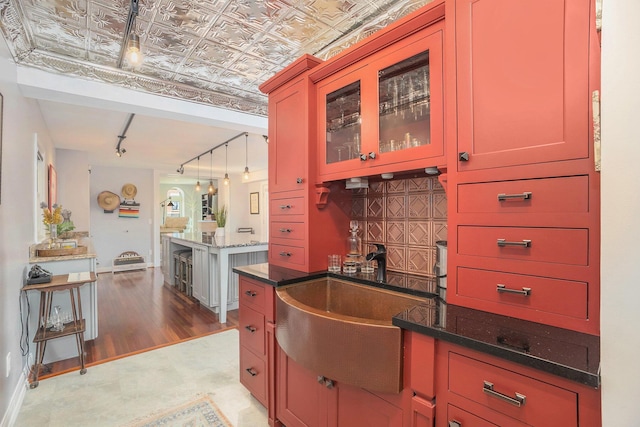 kitchen featuring track lighting, a sink, dark stone countertops, an ornate ceiling, and baseboards